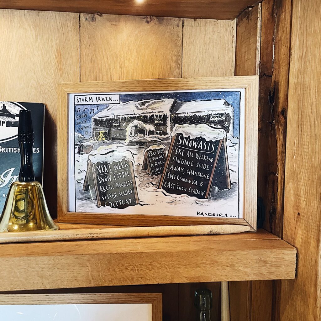 photo of a painting at the tan hill inn of the pub covered in snow. sandwich boards advertising snoasis, arctic monkeys and snow patrol bands